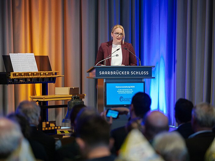 Urkundenverleihung_25_Streichert-Clivot Kulturministerin des Saarlands Streichert-Clivot hält Rede hinter einem Pult auf der Bühne.