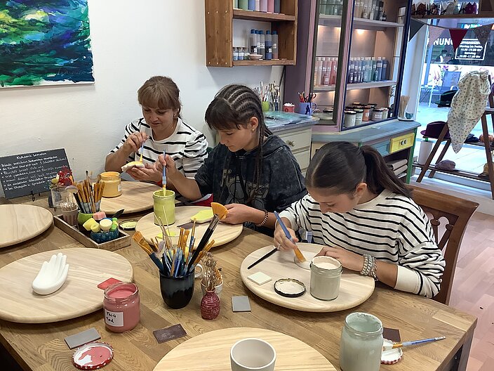 Workshop: Keramik bemalen © Herder-Gymnasium Minden Drei Personen sitzen an einem Tisch in einem Kunstatellier und bemalen Keramik