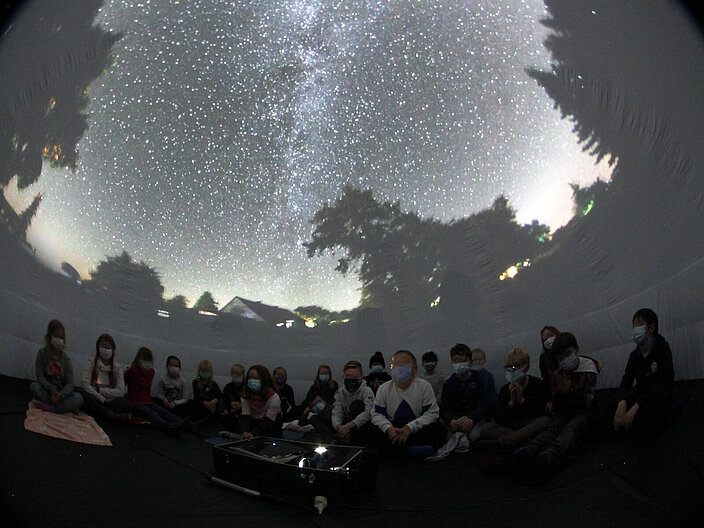 Im Inneren eines mobilen Planetariums sitzt eine Schulklasse auf dem Boden. Mobile Planetarien sind vergleichbar mit festinstallierten Planetarien