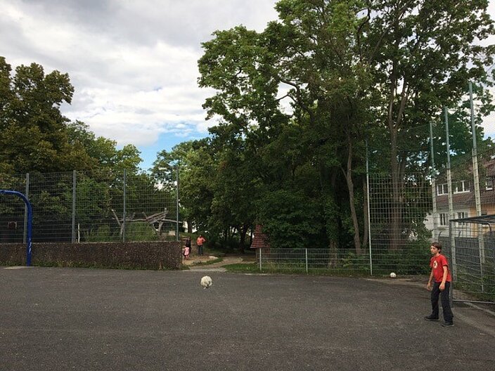 Ein Junge spielt Ball auf einem Bolzplatz.