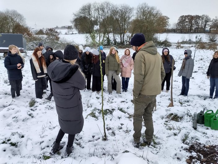 Recreation-Projekt 2023 in Tecklenburg - Pflanzen eines Friendsbaumes Eine Gruppe von Schülern steht im Schnee im Garten und pflanzt einen Friedensbaum.