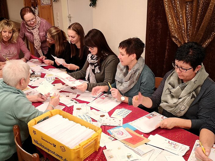 Freiwillige sitzen gemeinsam an einem langen Tisch und beantworten Kinderbriefe an den Nikolaus