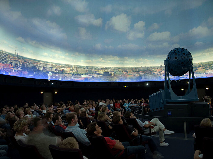 Menschen sitzen in einem Planetarium und warten auf die Vorführung.