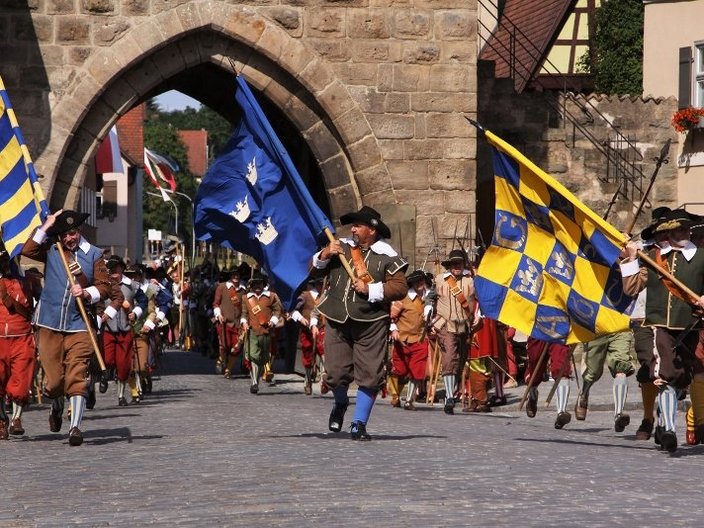 Männer mit Fahnen und historischen Kostümen vor einem Stadttor