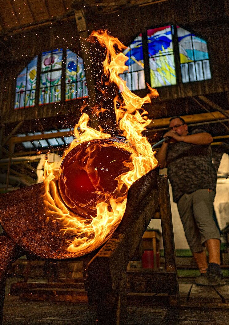 Glasmachermeister bläst eine Glaskugel auf, die umgeben von Feuer ist.