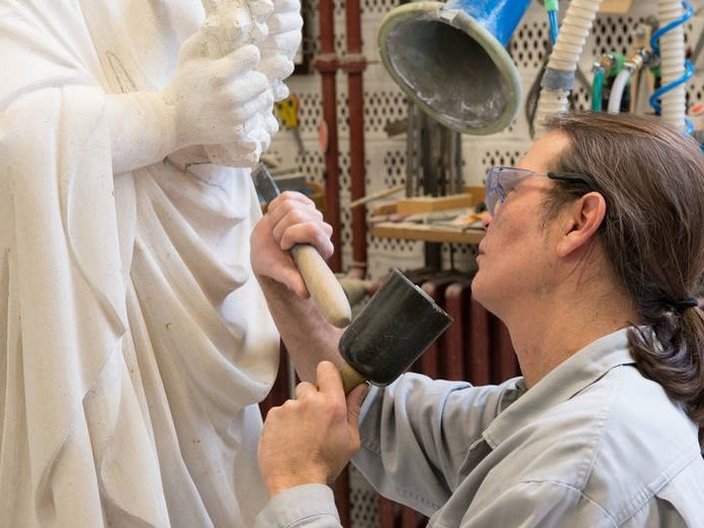 Handwerker beschlägt eine Statue mit Hammer und Meißel