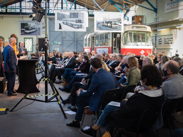 Die Teilnehmenden der Fachtagung schauen links auf die Redner des Eröffnungsabends. Im Hintergrund steht ein antiker Bahnwagon.