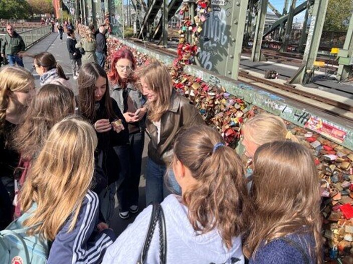 Stadt-Rallye durch Köln © Städt. Hansa-Gymnasium Köln Mehrere Personen stehen im Kreis und stecken die Köpfe zusammen. Im Hintergrund erkennt man eine Brücke in Köln.