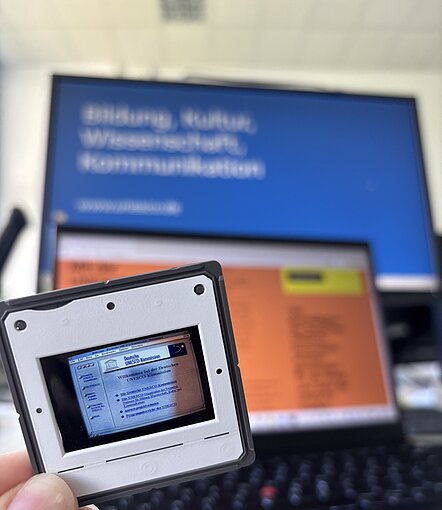 Ein Dia wird hochgehalten, darauf zu sehen ist die erste DUK-Website von 1996.