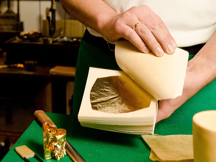Goldschlägermeister hält mit seinen Händen das ausgeschlagene Blattgold in der Schlagform in die Kamera. 