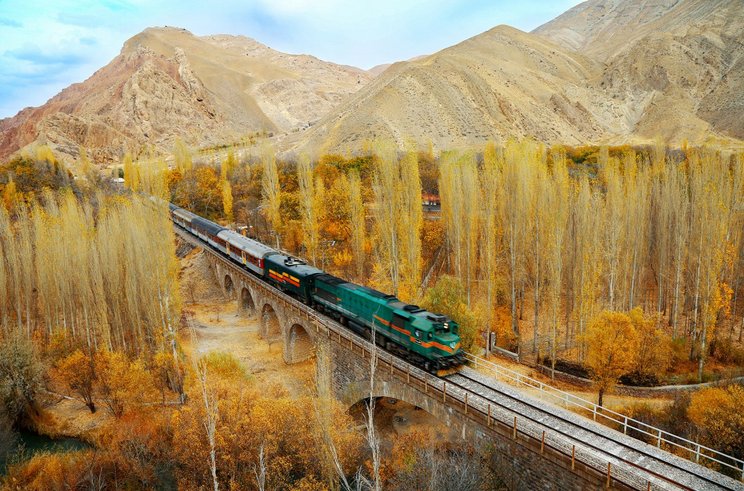 44whc_transiranische-eisenbahn_iran_c_hossein-javadi_0 Bahn fährt durch eine Gebirgs- und Waldlandschaft.