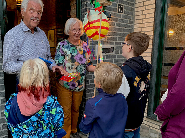 05_Martinsbräuche_heischebrauch_rene-bongartz Drei Kinder stehen am Hauseingang. Ein älteres Ehepaar steht in der Tür und hört den Kindern dabei zu. Ein Kind hat eine Laterne dabei.