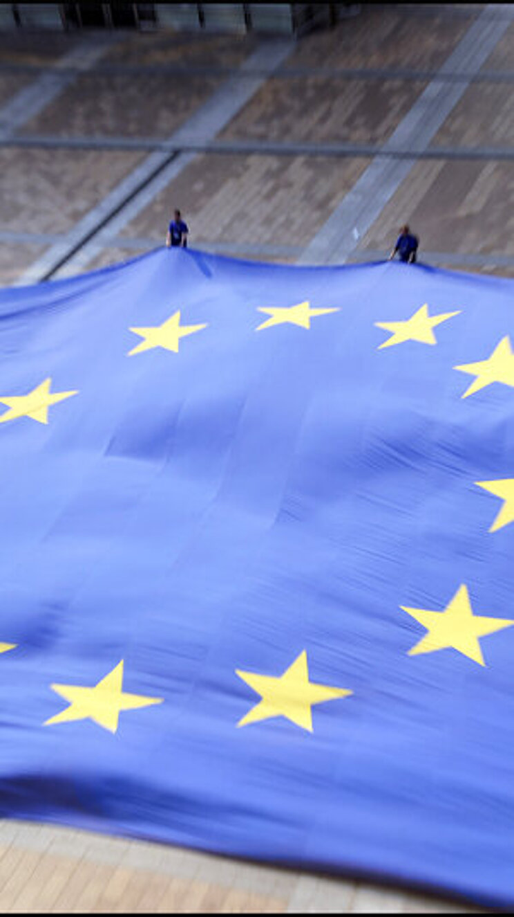 Viele Menschen spannen auf einem Platz eine übergroße Europaflagge auf.