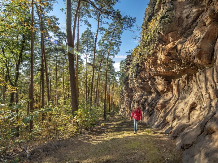 Eine Wanderin vor eine Felswand im Wald im Biosphärenreservat Pfälzerwald-Nordvogesen