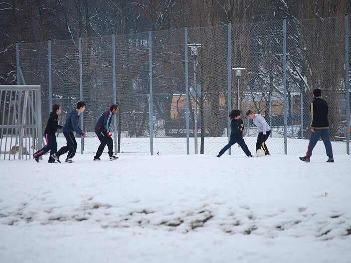 Bolzplatz im Schnee. Trotz Schnee spielt eine Gruppe von Jugendlichen Fu&szlig;ball