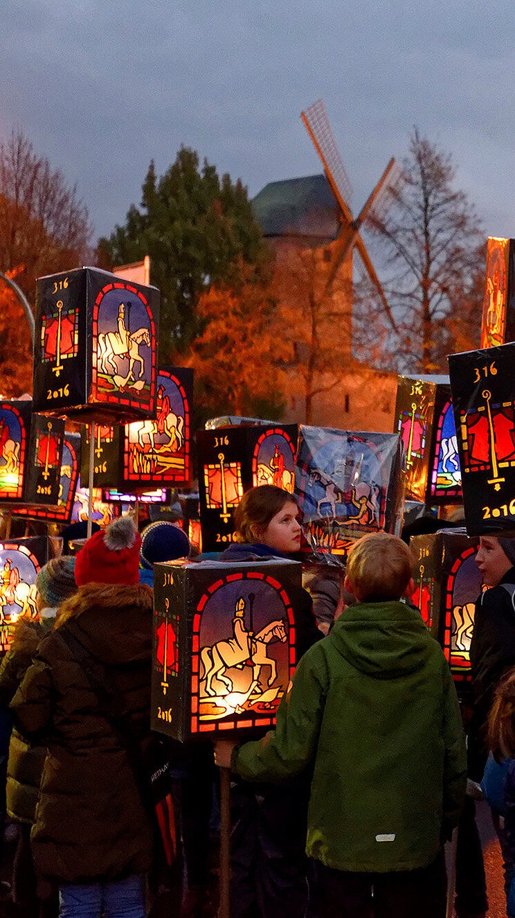 Kinder stehen auf der Stra&szlig;e im Halbdunklen und halten ihre Laternen in der Hand. Auf allen Laternen ist St. Martin auf einem Pferd abgebildet