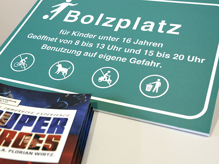 Ein gr&uuml;nes Schild mit der Aufschrift Bolzplatz liegt auf einem Tisch