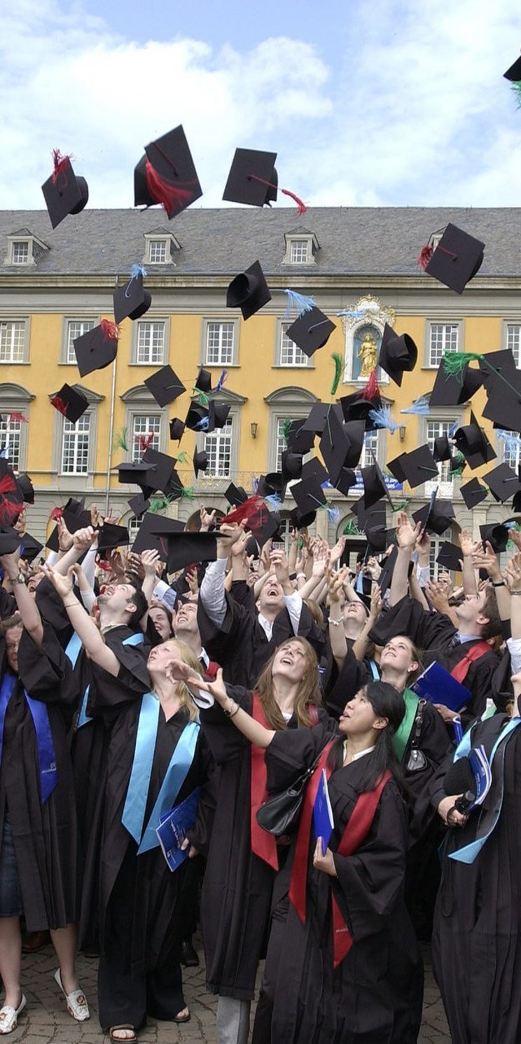 Absolventinnen und Absolventen werfen ihre Hüte vor der Universität Bonn in die Luft.