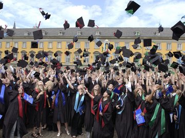 Absolventinnen und Absolventen werfen ihre Hüte vor der Universität Bonn in die Luft.