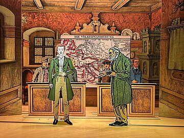 Historisch gestaltete Museums- oder Dioramaszene in einem holzverkleideten Raum. Im Vordergrund stehen zwei ausgeschnittene Figuren in historischer Kleidung vor Holztischen. Im Hintergrund befindet sich eine gro&szlig;e Karte mit der &Uuml;berschrift &bdquo;Die V&ouml;lkerwanderung&ldquo;, auf der Wanderungsbewegungen in Europa eingezeichnet sind. Weitere Figuren sind im Raum verteilt. Die Einrichtung umfasst verzierte rote Tapeten, Holzbalken an der Decke, ein Fenster sowie einen kunstvoll gestalteten Kachelofen. Die Szene wirkt wie ein dreidimensionales Schaubild zur europ&auml;ischen Geschichte.