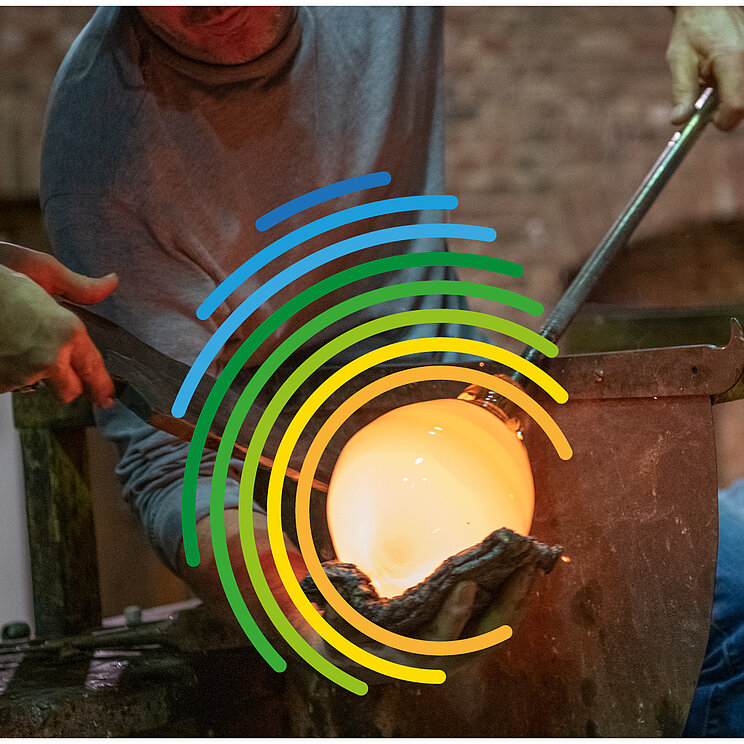 DUK_IKE_Fotowettbewerb_2026 In einer Glasbläserei bearbeiten mehrere Personen mit langen Metallrohren eine glühende Glasmasse. Im Vordergrund leuchtet eine kugelförmige Glasblase in einem Ofen. Über dem Motiv liegt das farbige Logo zum Welttag des Immateriellen Kulturerbes. Rechts ist der Schriftzug „Welttag des Immateriellen Kulturerbes“ zu sehen.