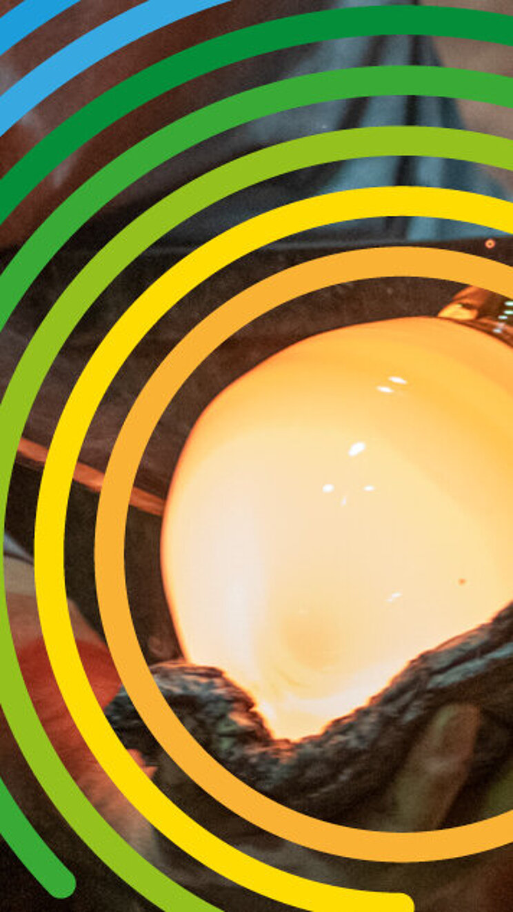 DUK_IKE_Fotowettbewerb_2026 In einer Glasbläserei bearbeiten mehrere Personen mit langen Metallrohren eine glühende Glasmasse. Im Vordergrund leuchtet eine kugelförmige Glasblase in einem Ofen. Über dem Motiv liegt das farbige Logo zum Welttag des Immateriellen Kulturerbes. Rechts ist der Schriftzug „Welttag des Immateriellen Kulturerbes“ zu sehen.