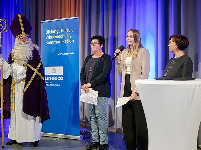 Urkundenverleihung_25_Nikolauspostamt Trägergruppe vom Nikolauspostamt auf der Bühne. Eine Person als Nikolaus verkleidet.