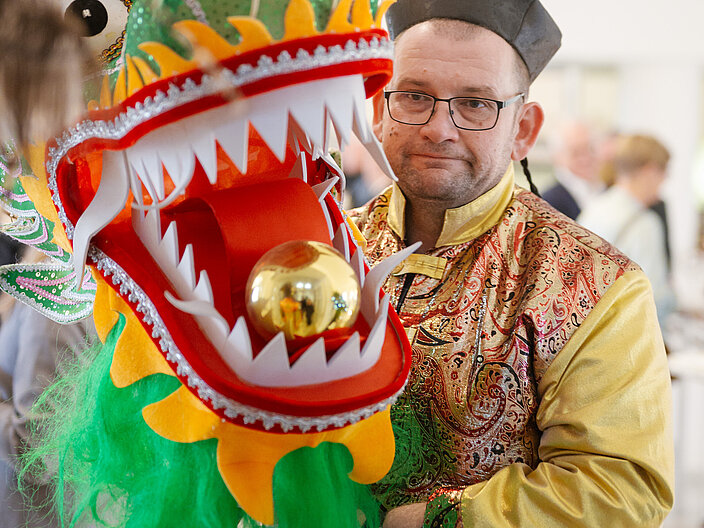 Urkundenverleihung_25_Chinesenfasching Träger des Chinesenfaschings mit einer Drachenkopffigur in der Hand.