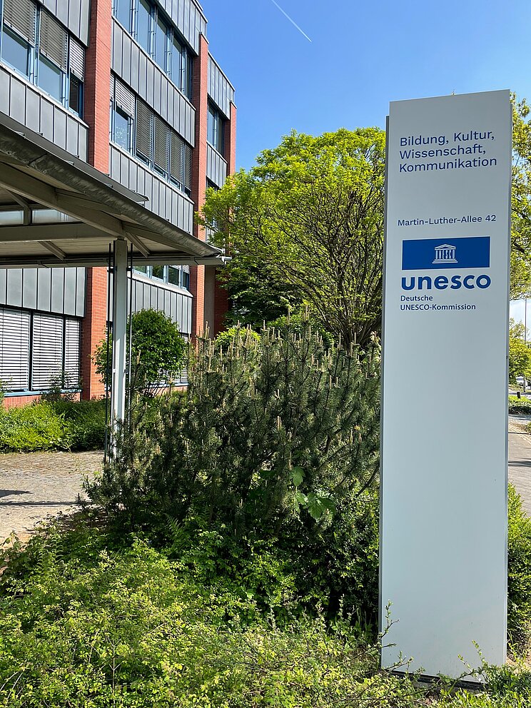 Stele mit UNESCO-Logo und Adresse vor DUK Gebäude Weiße Stele mit blauem UNESCO-Logo und Adresse vor dem DUK-Gebäude