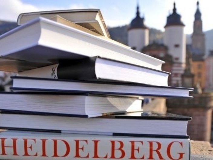 Ein Stapel Bücher liegt vor der Stadtsilhouette von Heidelberg im Hintergrund