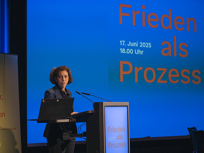 Frau am Rednerpult vor blauem Hintergrund