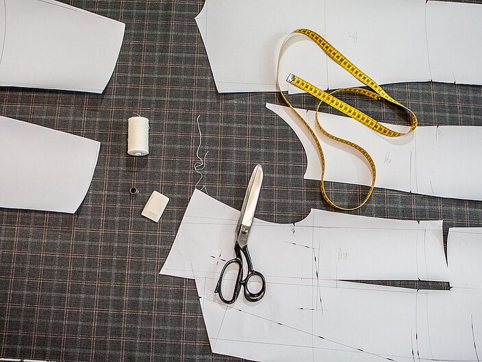 Auf einem Tisch liegen Schnittmuster, Stoff, Ma&szlig;band und Schere.