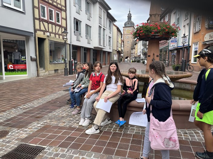 Mehrere Schüler und Schülerinnen sitzen auf einem Brunnen in der Innenstadt von Buchen.