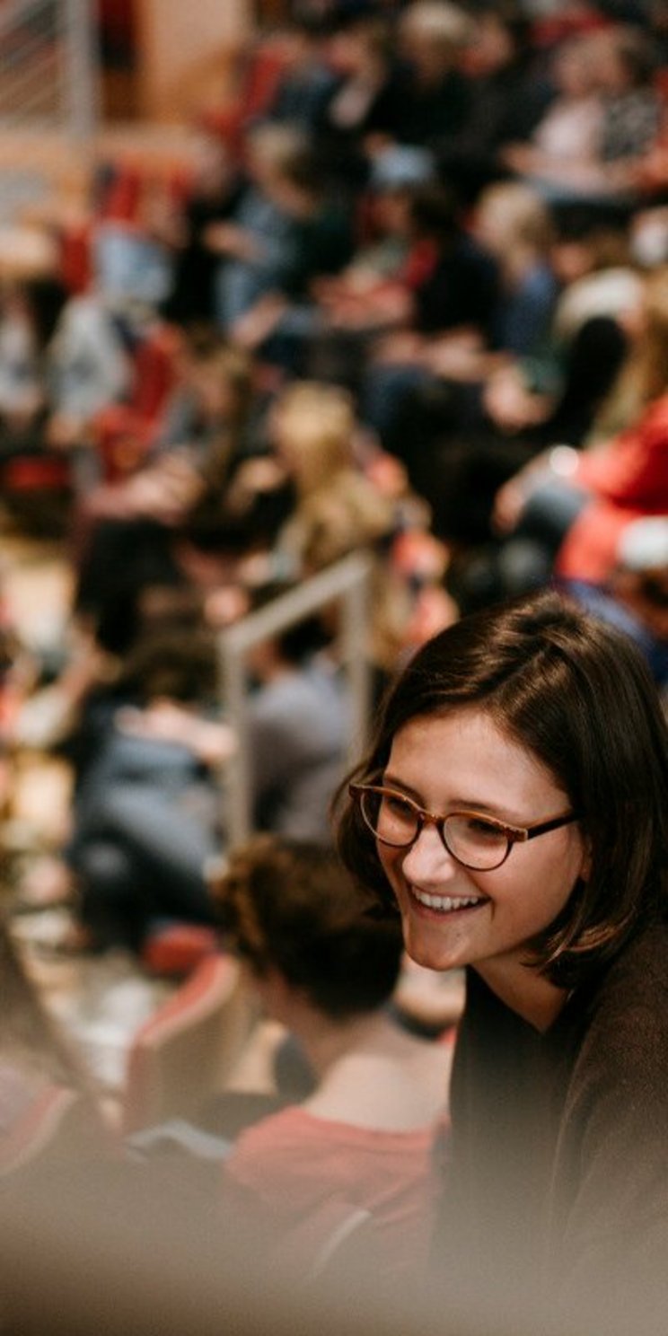 Eine junge Frau in einem Hörsaal einer Hochschule.