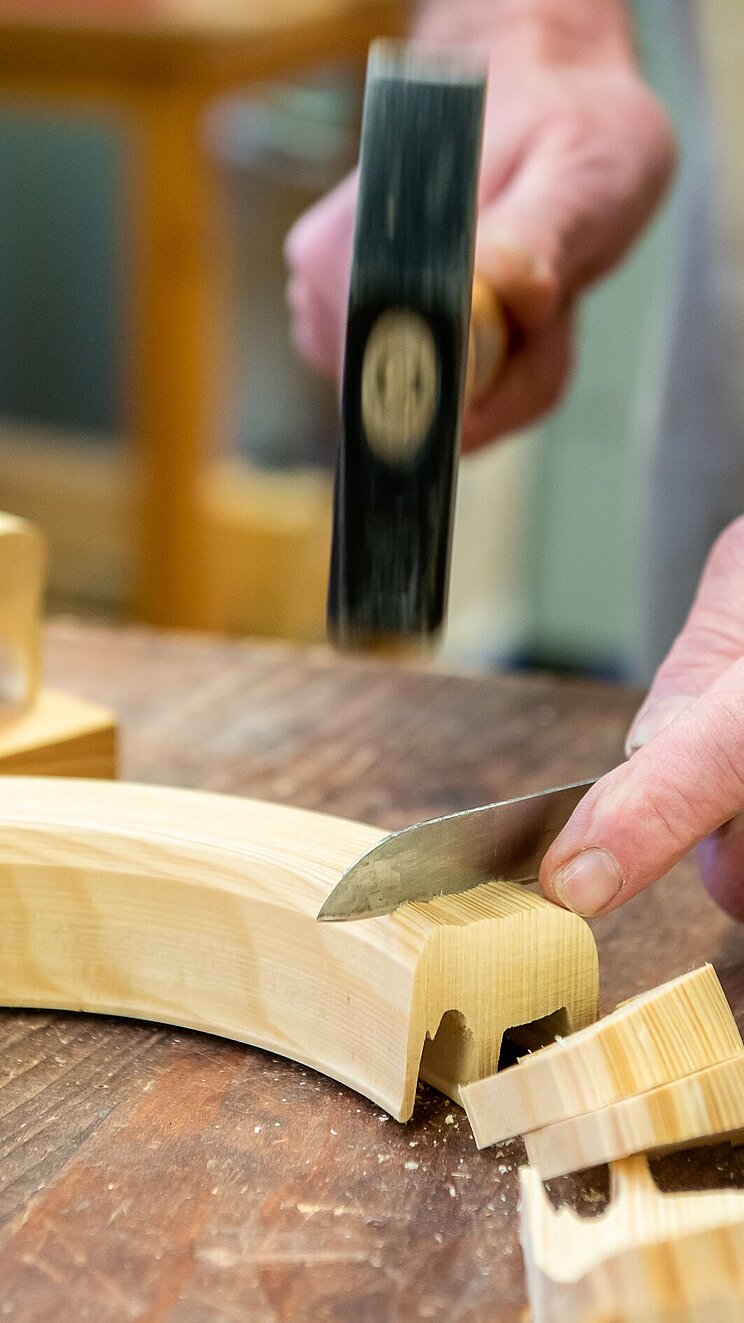 Mit einem Messer und Hammer werden aus einem Holzbogen Holzfiguren herausgebrochen.