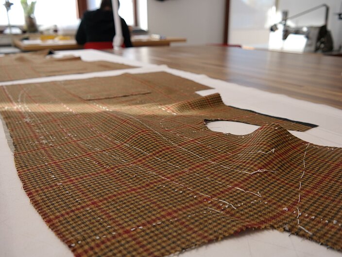 Auf einer Werkbank ist ein ausgeschnittenes und unterschlagenes Vorderteil eines Anzugs ausgebreitet.