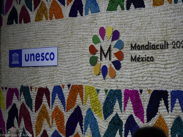 Bunt gestaltete Wand mit dem Logo der UNESCO und der Weltkulturkonferenz Mondiacult 2022. 