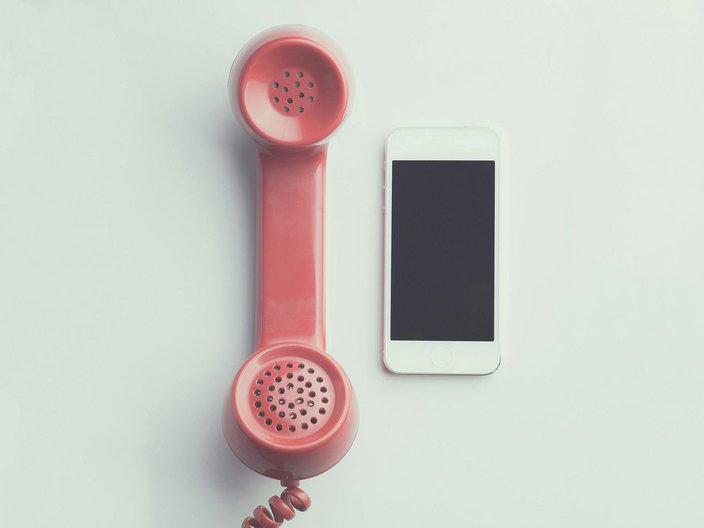 Blick auf einen alten Telefonhörer mit Kabelschnur und einem Smartphone, die nebeneinander liegen.