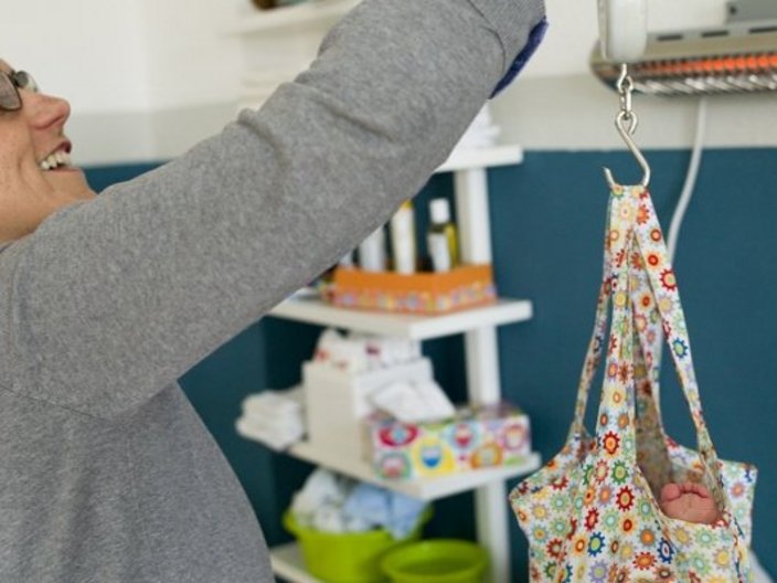 Hebamme wiegt Baby in einer Stofftasche
