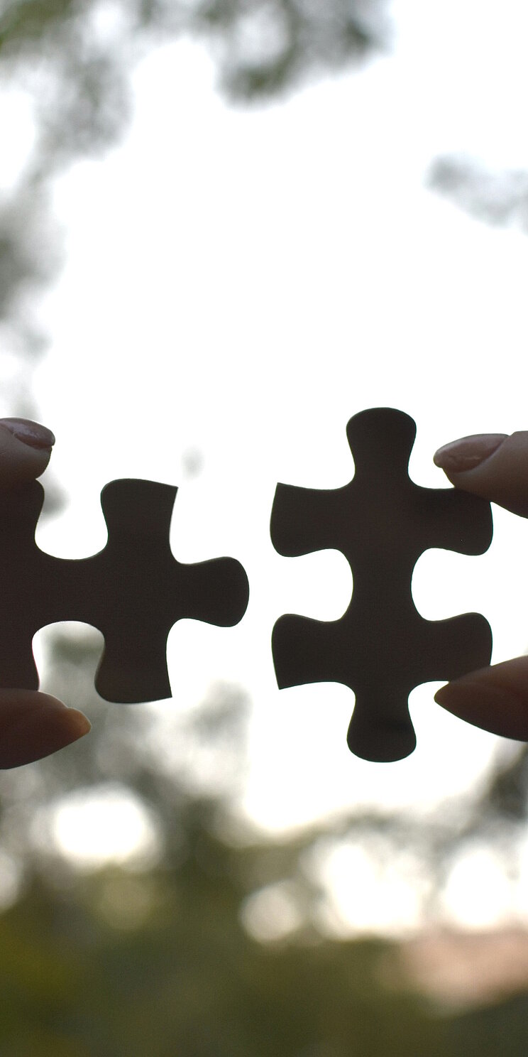 Zwek Hände, die Puzzleteile gegen den Himmel zusammen fügen