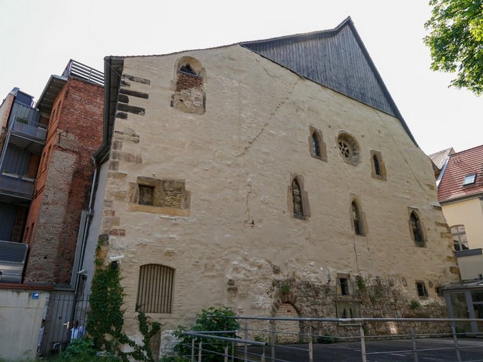 Das Bild zeigt die Fassade eines mehrstöckigen Gebäudes, die mit Fenstern verschiedener Form und Größe bestückt ist. 