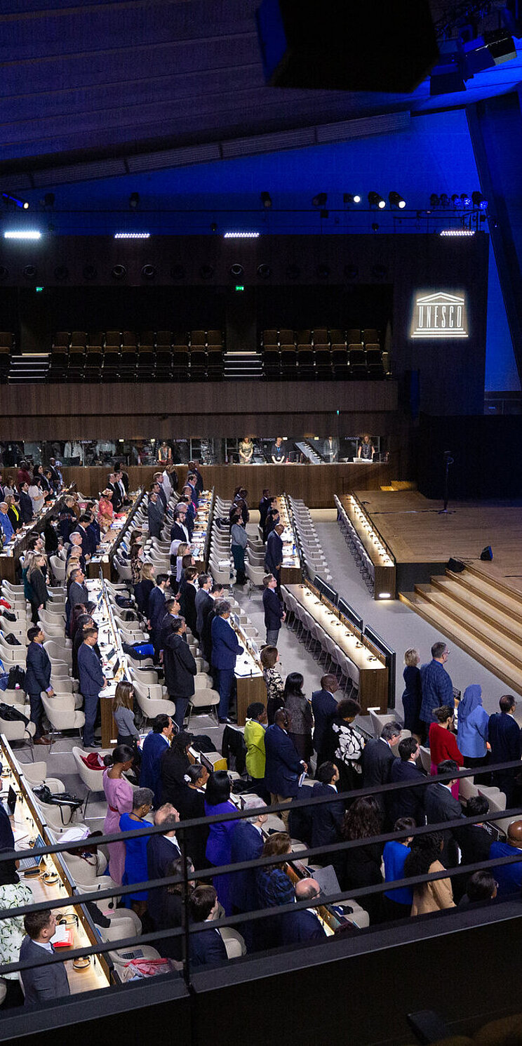 Blick in einen voll besetzten Konferenzsaal. Das Podium befindet sich auf der rechten Seite.