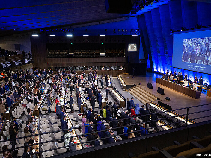 Blick in einen voll besetzten Konferenzsaal. Das Podium befindet sich auf der rechten Seite.