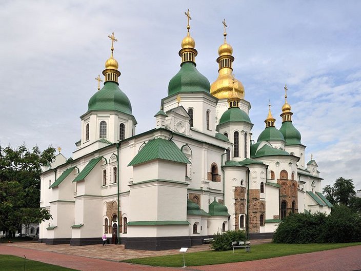 Die UNESCO-Welterbestätte Sophienkathedrale in der Ukraine von der Seite fotografiert. Ein weißes sakrales Gebäude mit grünen Kuppel und vergoldeten Soitzen.
