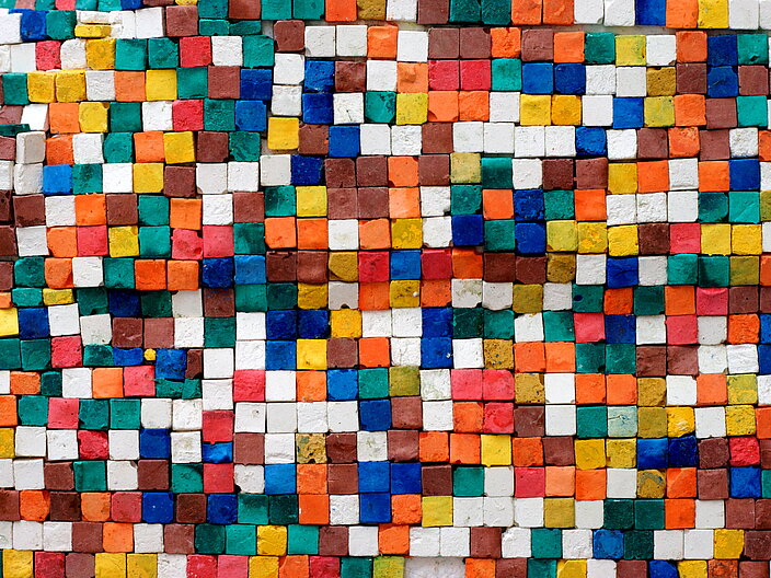 Das Bild zeigt ein Mosaik aus kleinen bunten Steinen, die ein abstraktes Muster ergeben.