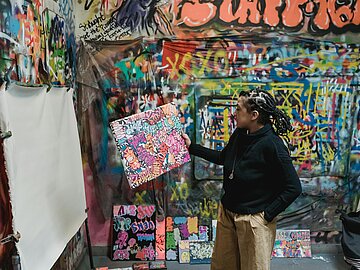 Künstlerin_Pexels_Felicity Tai Künstlerin mit bemalter Leinwand in einem Raum voller Kunst