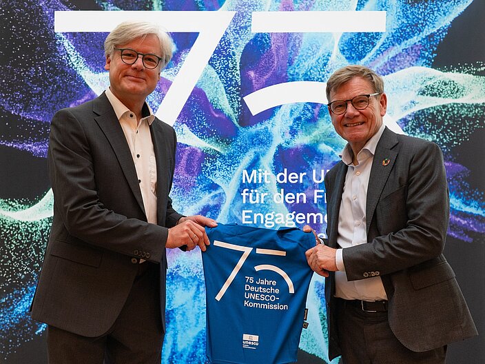 Roman Luckscheiter und Johann Wadephul beim Tag der offenen Tür im Auswärtigen Amt 2026 Roman Luckscheiter und Johann Wadephul halten zusammen den Beutel zum Jubiläum der Deutschen UNESCO-Kommission hoch