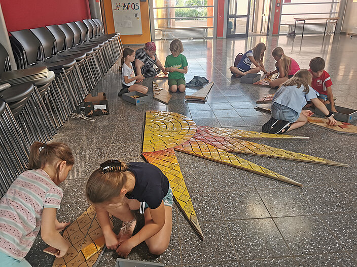 Kinder gestalten in Zusammenarbeit mit Töpfern ein Keramik-Wandbild in ihrer Schule. 