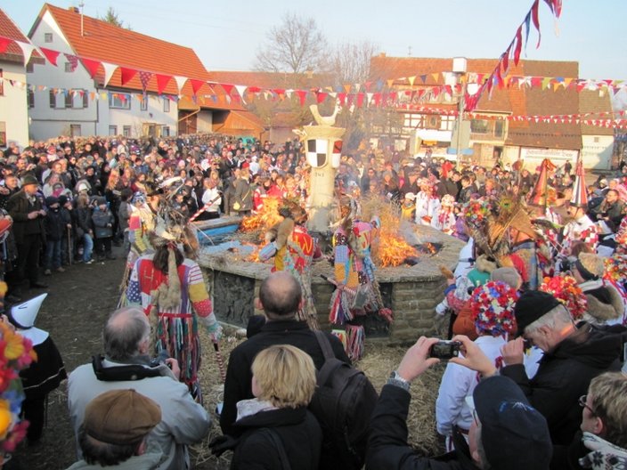Kostümierte Personen tanzen um einen Brunnen