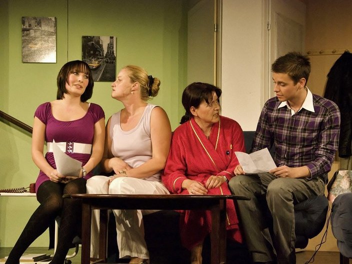 Gruppe von Schauspielern sitzen um einen Tisch auf einer Bühne